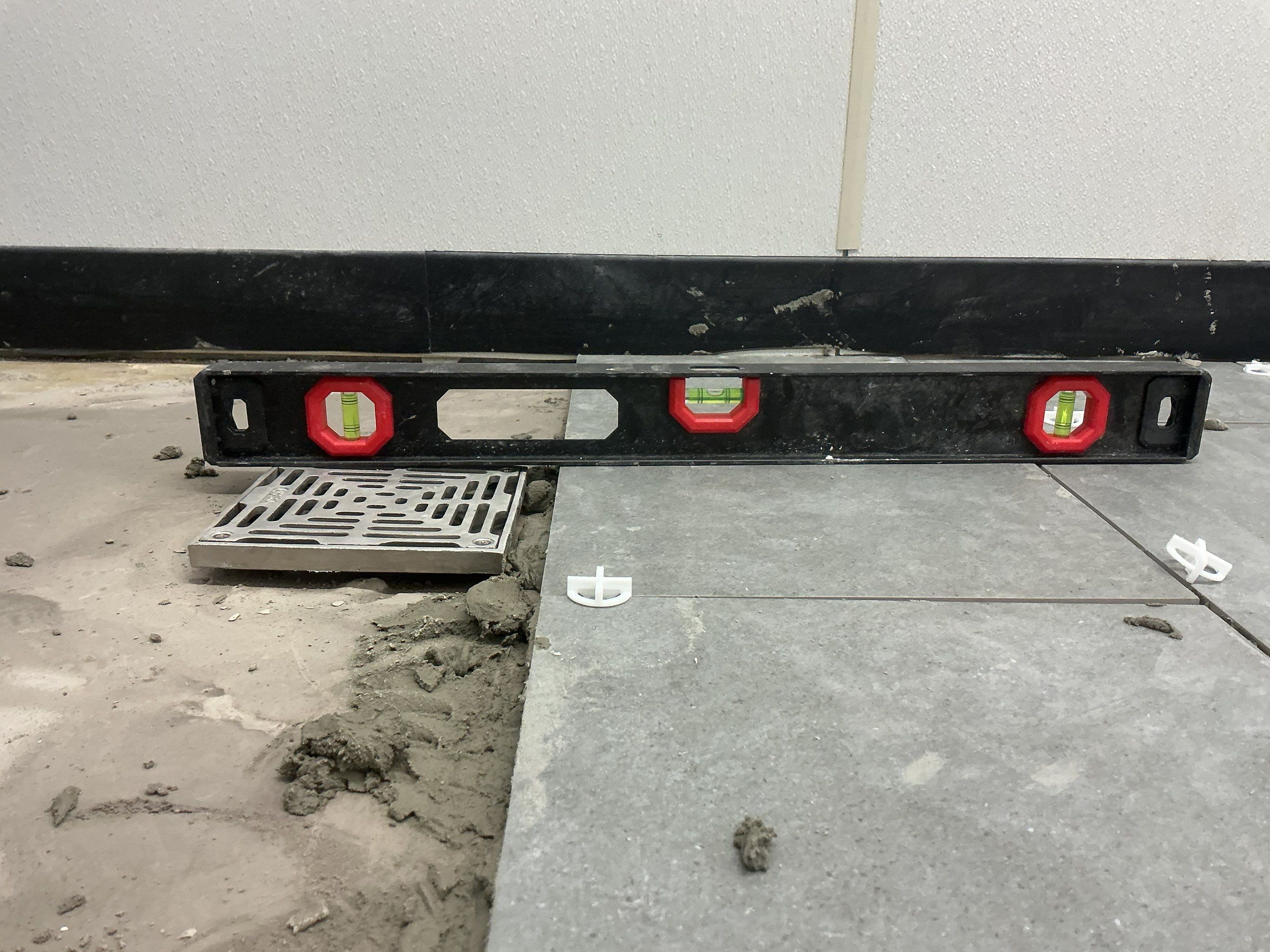 Ceramic restroom floor tile being leveled around a drain with spacers