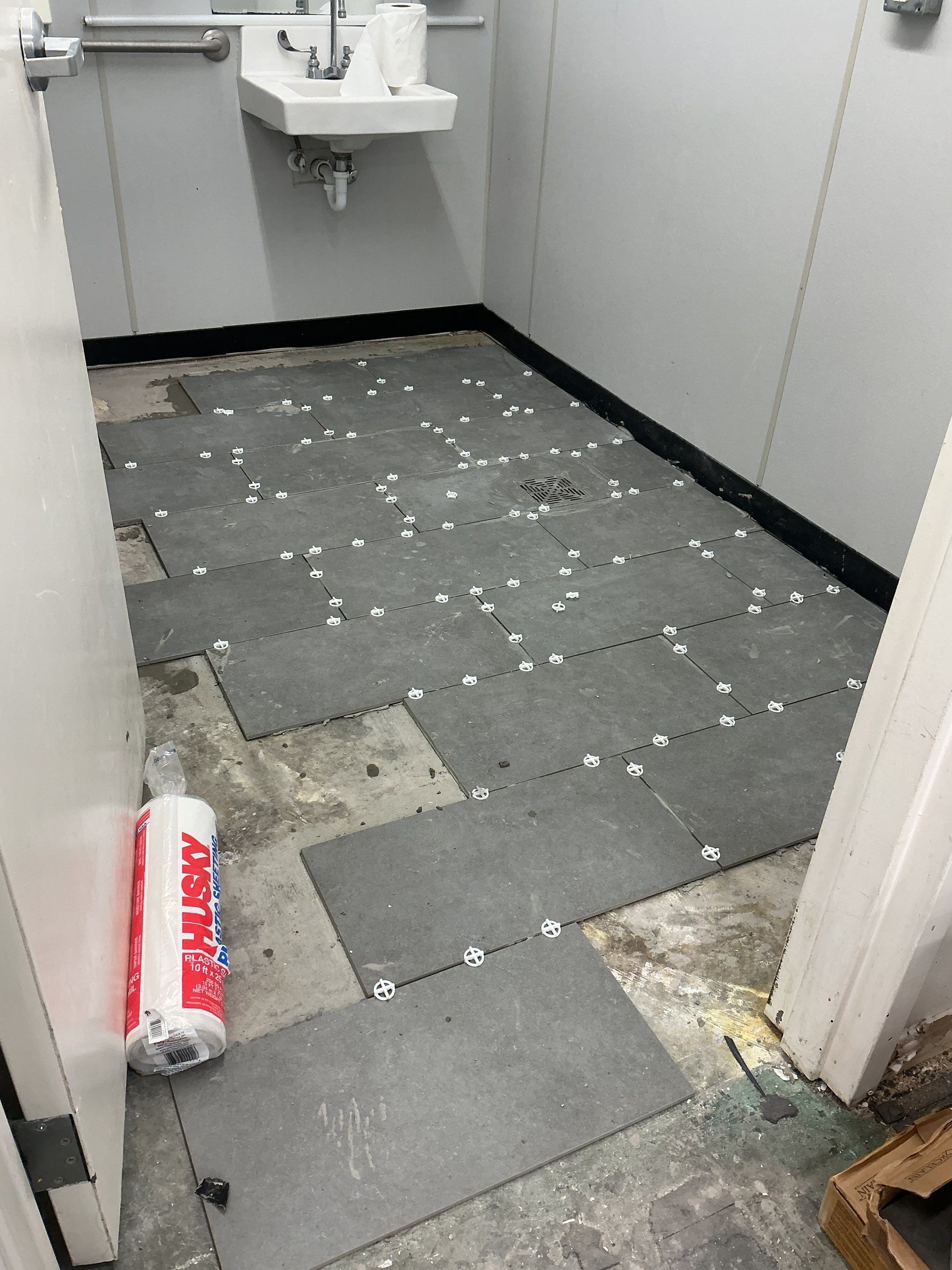 Large-format ceramic restroom tile laid out with leveling spacers